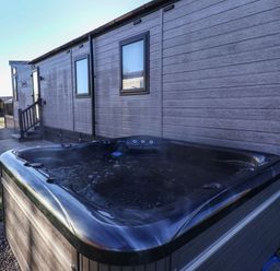 An outdoor hot tub next to a grey wooden cabin with windows at Owl's Nest in Newton on Derwent near Wilberfoss