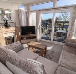 A living room with couches a coffee table a TV a fireplace and glass doors leading to a deck at Owl's Nest in Newton on Derwent near Wilberfoss