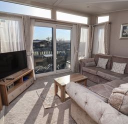 A living room with a sectional sofa a wooden coffee table a flat screen tv on a wooden stand sliding glass doors leading to an outdoor patio at Owls Nest in Newton on Derwent near Wilberfoss