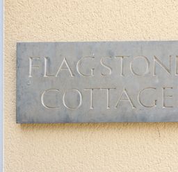 A metal sign with the text flagstone cottage on a textured beige wall at Flagstone Cottage Upper Swell near Stow-On-The-Wold