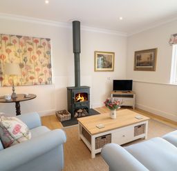 A living room with a wood burning stove a television on a stand two sofas and a coffee table at Flagstone Cottage in Upper Swell near Stow-On-The-Wold