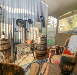 A seating area with wooden barrel chairs, a wood stove, and two barrels used as tables at The Wagon at Burrow Hill in Ottery St Mary