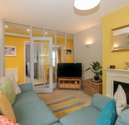 A living room with blue sofas, a TV on a wooden stand, a fireplace, and a glass door at The Lobster Pot in Overstrand