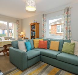 A living room with a blue corner sofa and colorful cushions near a dining table with chairs at The Lobster Pot in Overstrand