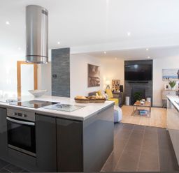 A modern kitchen with an island and oven next to a living area with a sofa and TV at Hafod Heli in Rhosneigr