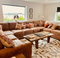 A living room with a large brown sectional sofa and a wooden coffee table with a chess set at Hafod Heli in Rhosneigr
