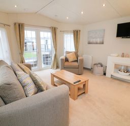 A living room with a sofa a chair coffee table television and glass doors at The Bobbin Number 11 South Lakeland Leisure Village near Carnforth