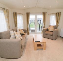 A living room with a sofa armchair coffee table and windows with curtains at The Bobbin Number 11 South Lakeland Leisure Village near Carnforth