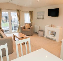 A living room with sofa armchair coffee table wall mounted TV and sliding glass doors at The Bobbin Number 11 South Lakeland Leisure Village near Carnforth