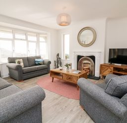 A living room with gray sofas a wooden coffee table a round rug a fireplace and a television at Greenbank in Woolacombe