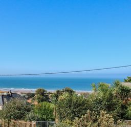 A coastal view of houses with plants and trees in the foreground and the ocean in the background at Greenbank in Woolacombe
