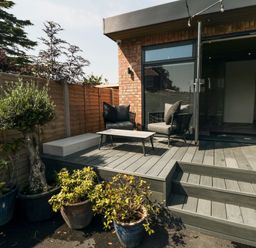 An outdoor wooden deck with two chairs a table and potted plants at Nightingales in Bridlington