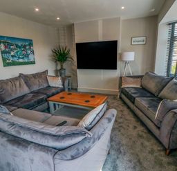 A living room with two grey sofas a wooden coffee table a wall-mounted TV a floor lamp a potted plant and a painting on the wall at Nightingales in Bridlington