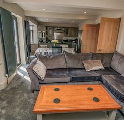 A living room with a grey sectional sofa a wooden coffee table and an open doorway to a kitchen with a dining table and chairs at Nightingales in Bridlington