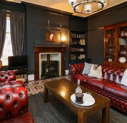 A living room with red leather sofas a fireplace a wooden cabinet and a glass coffee table at Tirallen in Llangadog