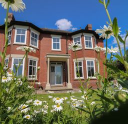 A brick house with white framed windows and daisies in the front garden at Tirallen in Llangadog