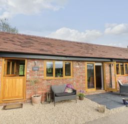 A brick building with wooden doors and windows and outdoor seating at The Old Piggery in Defford