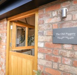 Half wooden door open on a brick wall with a sign reading The Old Piggery at The Old Piggery in Defford