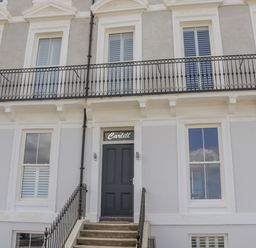 The front entrance of a building with stairs leading to a black door with the word Carlill above and windows on both sides Foxton Penthouse Whitby