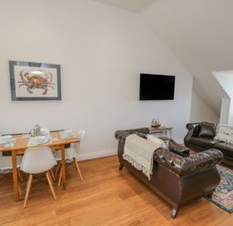 A dining table with four chairs set with plates and cutlery next to two brown leather sofas and a wall-mounted TV at Foxton Penthouse in Whitby