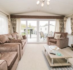 A living room with a brown sofa and armchair a wooden coffee table and large glass doors at Number 10 in Warton