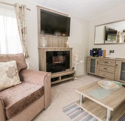 A living room with an armchair a TV mounted over an electric fireplace a sideboard with a stereo and a coffee table at Number 10 in Warton