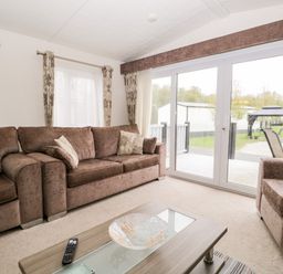 A living room with brown sofas and a coffee table facing sliding glass doors at Number 10 in Warton