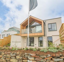 A modern two-story house with wood and glass balcony and stone retaining wall at Porth Beach in Porth near St Columb Minor