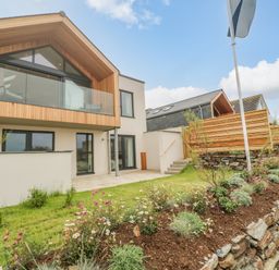Exterior of a modern two-story house with a wooden balcony and garden at Porth Beach in Porth near St Columb Minor