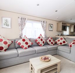 A living room with a gray sectional sofa with red and white patterned cushions a wooden coffee table and framed pictures on the wall at Freddy's Lodge Foxburrow Hang in Fritton
