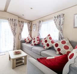 A living room with a grey sofa with red and white cushions a wooden coffee table and floral curtains at Freddy's Lodge Foxburrow Hang in Fritton