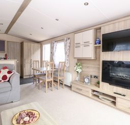 A living room with a sofa and dining table near a TV and electric fireplace at Freddy's Lodge Foxburrow Hang in Fritton