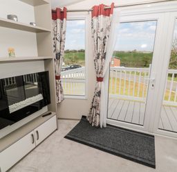 A room with glass doors leading to a balcony with railings shelves with decorative items and a fireplace at Moonlight Lodge in Bockenfield Country Holiday Park near West Thirston