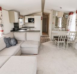 A living room with a beige sofa and pillows next to a kitchen with white cabinets and a dining table with chairs at Moonlight Lodge in Bockenfield Country Holiday Park near West Thirston