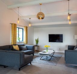 A living room with two gray sofas a coffee table with flowers a wall-mounted tv and hanging pendant lights at Quantock Barn in Stockland near Honiton