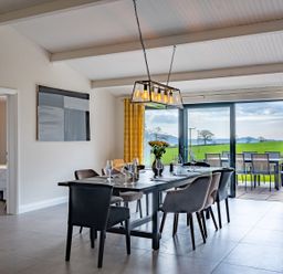 A dining room with a table set for six and sliding glass doors opening to a patio at Quantock Barn in Stockland near Honiton