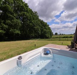 An outdoor hot tub on a patio next to a lawn with trees and a cloudy sky at Quantock Barn in Stockland near Honiton