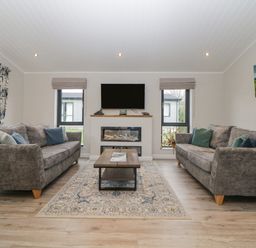 A living room with two grey sofas a wooden coffee table and a wall-mounted television at Meadow Lodge in Lifton