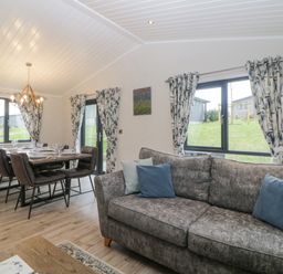 A living room with a gray sofa and a dining area with a table and six chairs at Meadow Lodge in Lifton