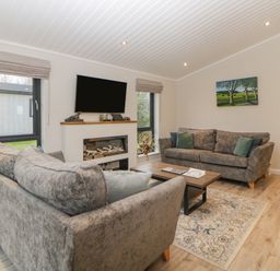 A living room with two sofas a coffee table a wall-mounted television and a fireplace at Meadow Lodge in Lifton