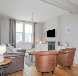 A living room with leather chairs a sofa a wall-mounted TV and windows at Cobblers Cottage in Beaumaris