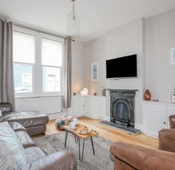 A living room with leather sofas a wooden coffee table a wall-mounted TV and a fireplace at Cobblers Cottage in Beaumaris