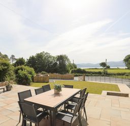 An outdoor patio with a dining table and chairs a seating area a lawn and countryside views at The Stables in Penmon near Beaumaris