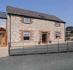 An exterior view of a stone and brick house with a small black fence and a gravel driveway at The Stables in Penmon near Beaumaris