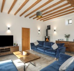 A living room with blue sofas wooden furniture a wood burning stove and exposed ceiling beams at The Stables in Penmon near Beaumaris