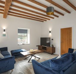 A living room with blue sofas wooden coffee table TV and exposed wooden ceiling beams at The Stables in Penmon near Beaumaris