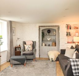 A living room with armchair ottoman sofa bookshelf and lamp at Hope Cottage in Buckfastleigh