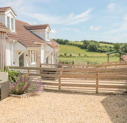 An outdoor patio area with a table and chairs beside a house with a wooden fence and green fields in the background at Garland in Nottington near Weymouth