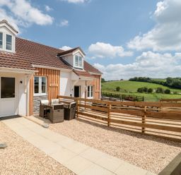 A house with outdoor seating and wooden fences overlooking green fields at Mellstock in Nottington near Weymouth