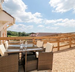 An outdoor patio area with a glass table and four chairs surrounded by a wooden fence at Mellstock Nottington near Weymouth